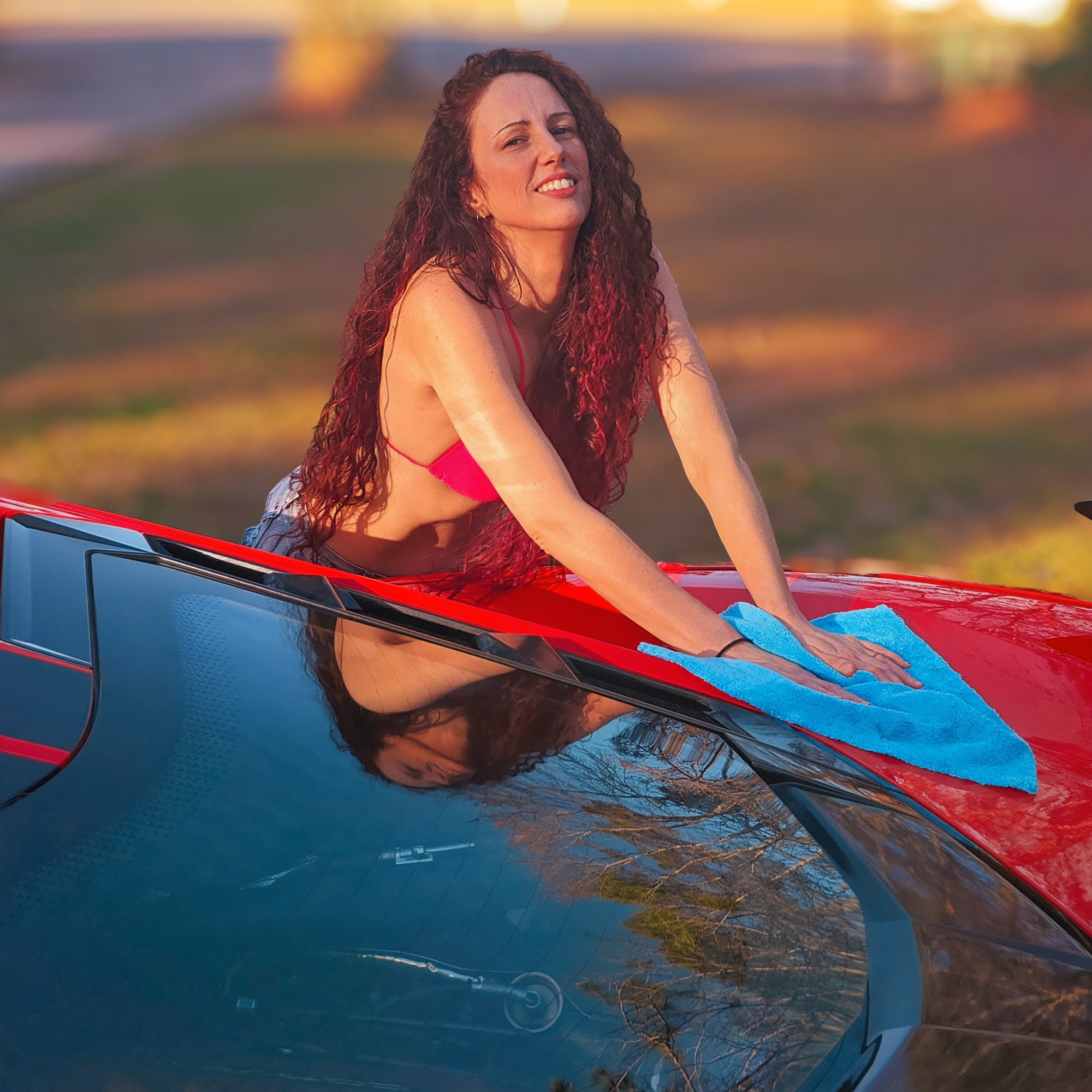 Alice smiling while detailing a red car during golden hour