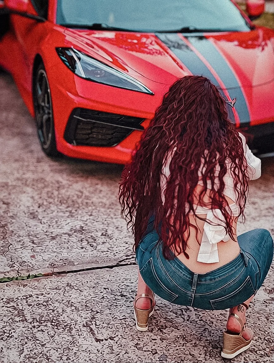 Alice crouched in front of her Torch Red Corvette, back turned, hair cascading down her shoulders